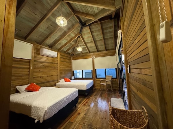 A wooden cabin with two beds, a chair, a small table, and a window with a view.