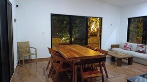 Un comedor con mesa y sillas de madera, un sofá y una ventana que da a vistas de vegetación.