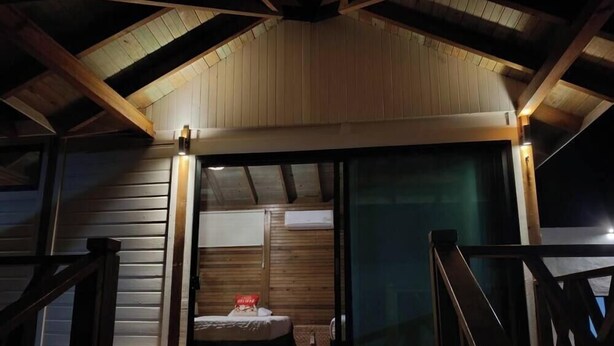 Una cabaña de madera con techo inclinado, una cama con almohada roja y una ventana con vistas.