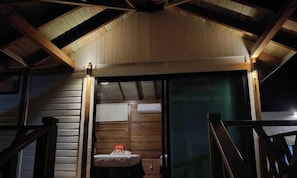 A wooden cabin with a sloped roof, a bed with a red pillow, and a window with a view.