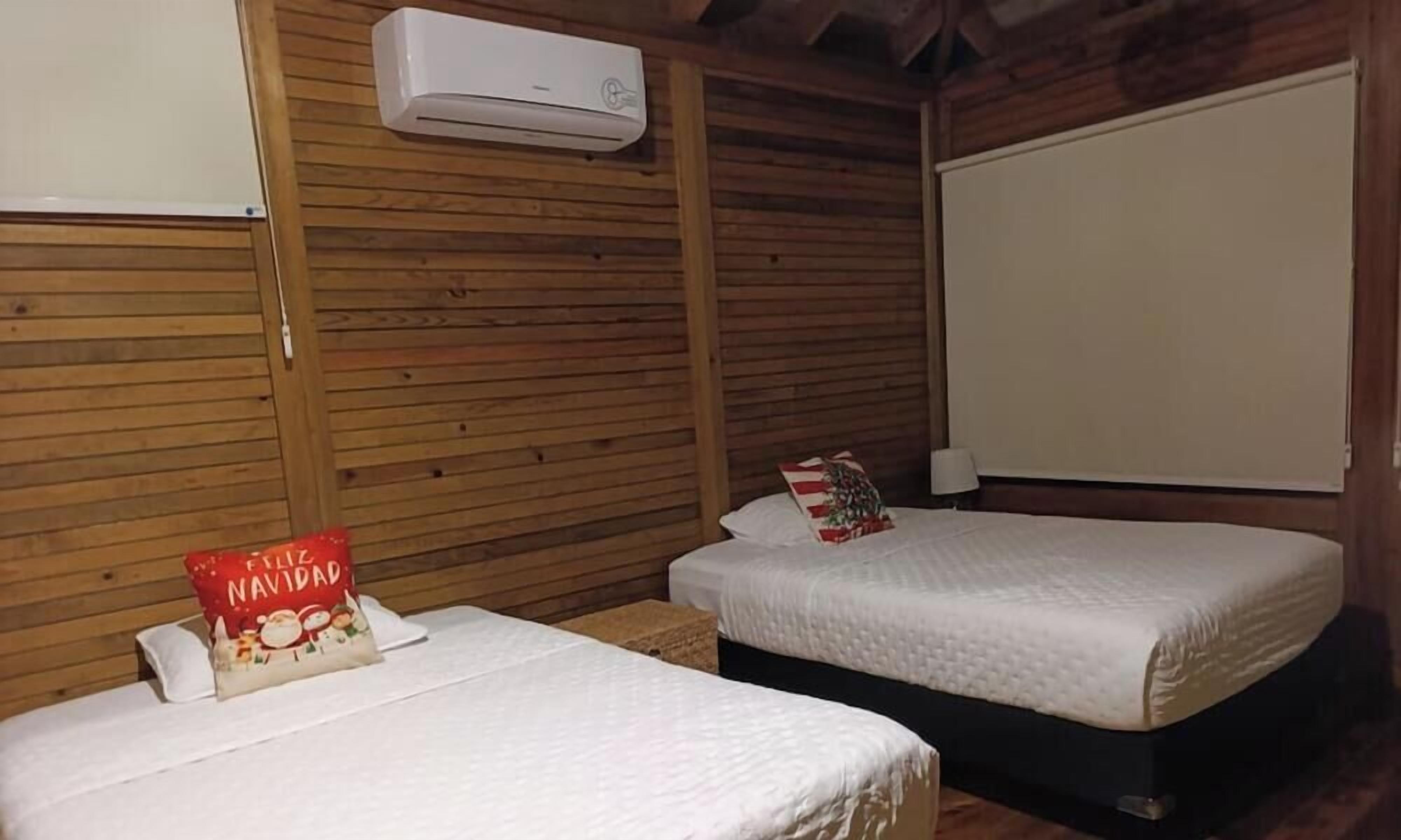 A room with two beds, wooden walls, an air conditioning unit, and a whiteboard.
