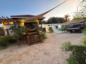A building with a wooden staircase leading to a covered area, surrounded by palm trees and a gravel driveway.