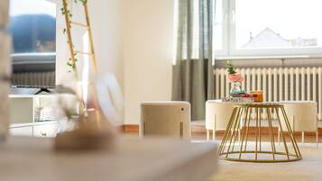 Ein modernes Wohnzimmer mit einer Couch, einem Couchtisch und Blick auf eine Stadtlandschaft durch große Fenster.