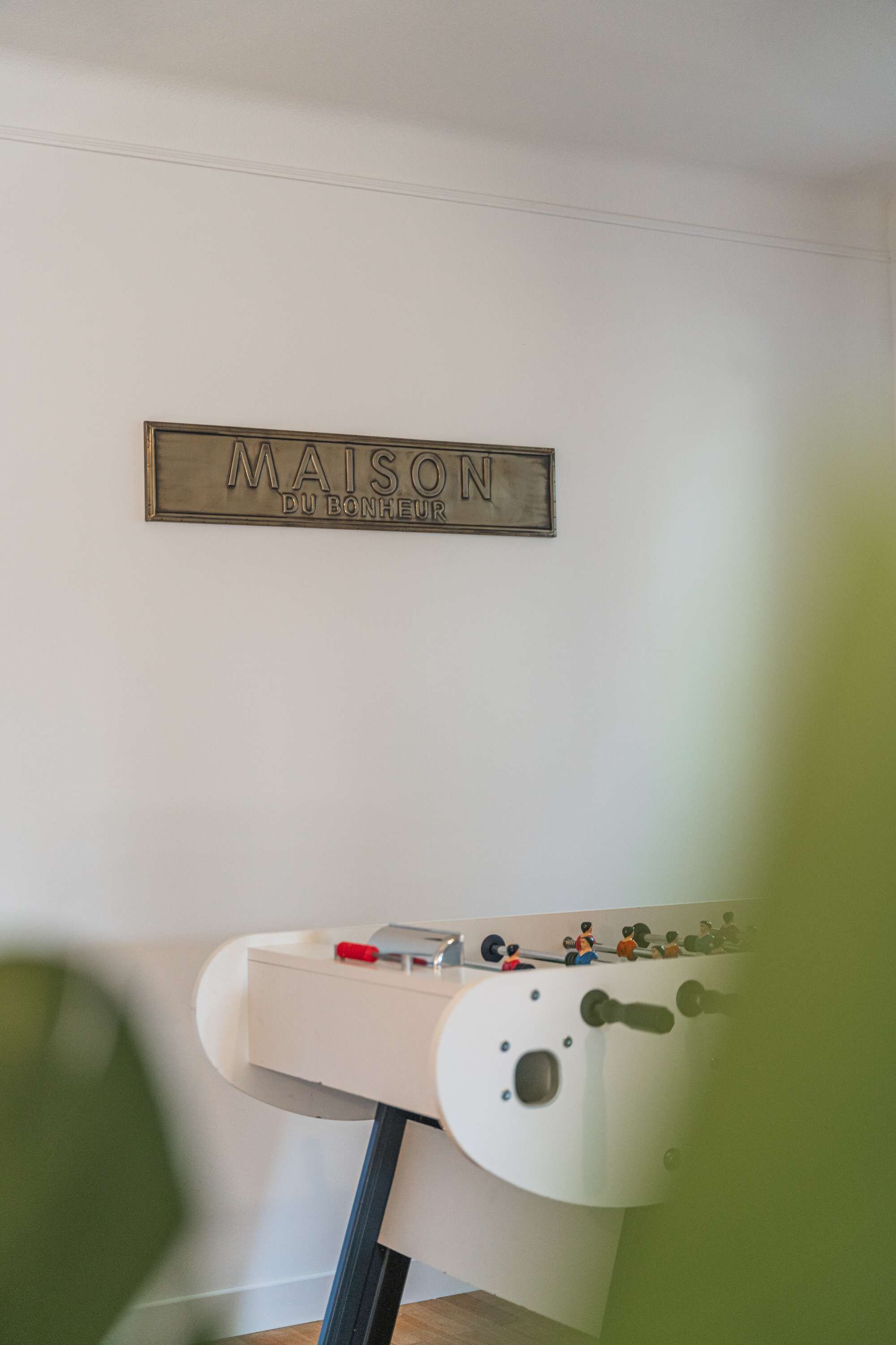 Un letrero en la pared que dice 'MAISON DU BONHEUR' y una mesa blanca con una mesa de fútbol.