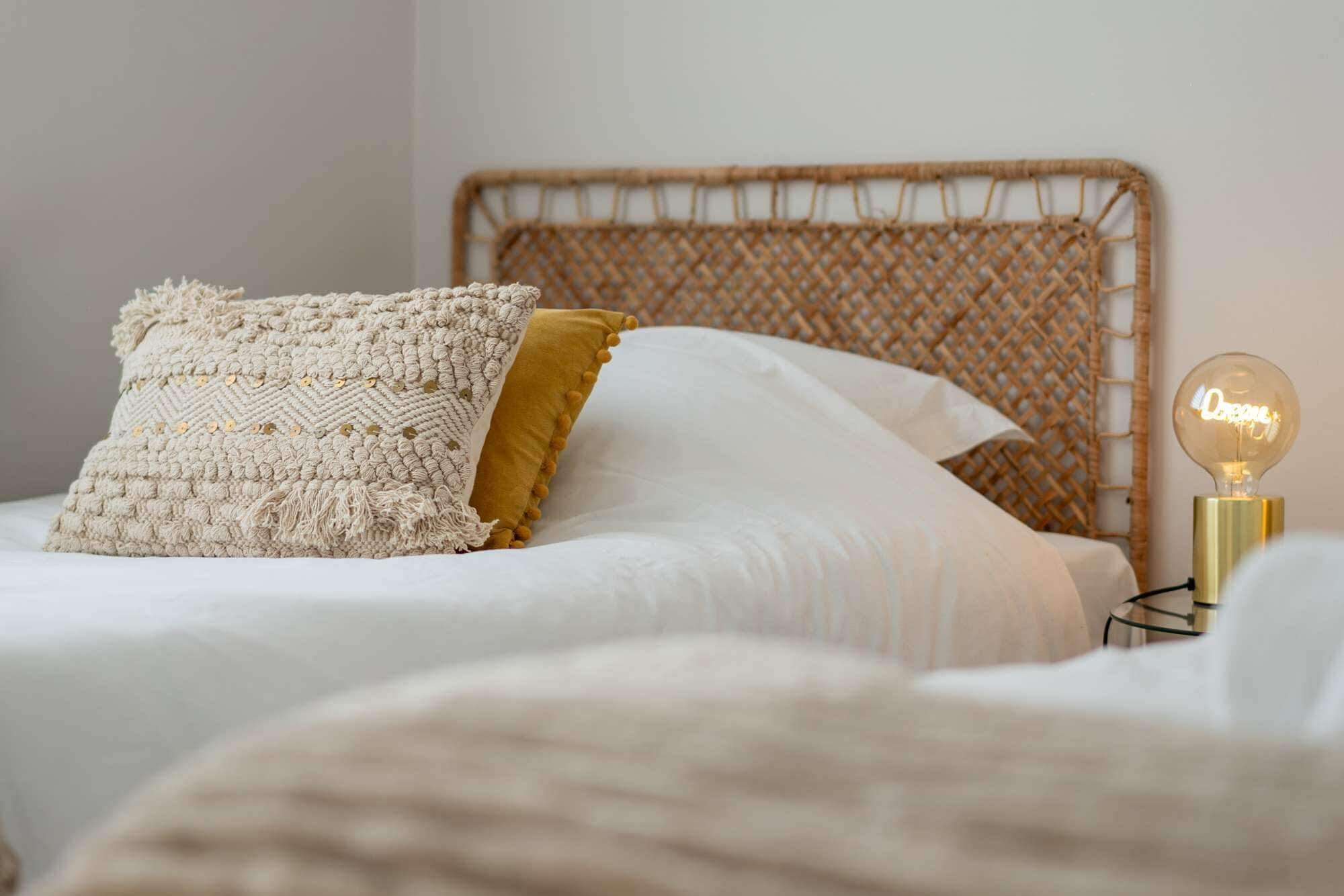 Cama com cabeceira de tear, almofada de macramé e uma almofada amarela mostarda, além de um abajur.