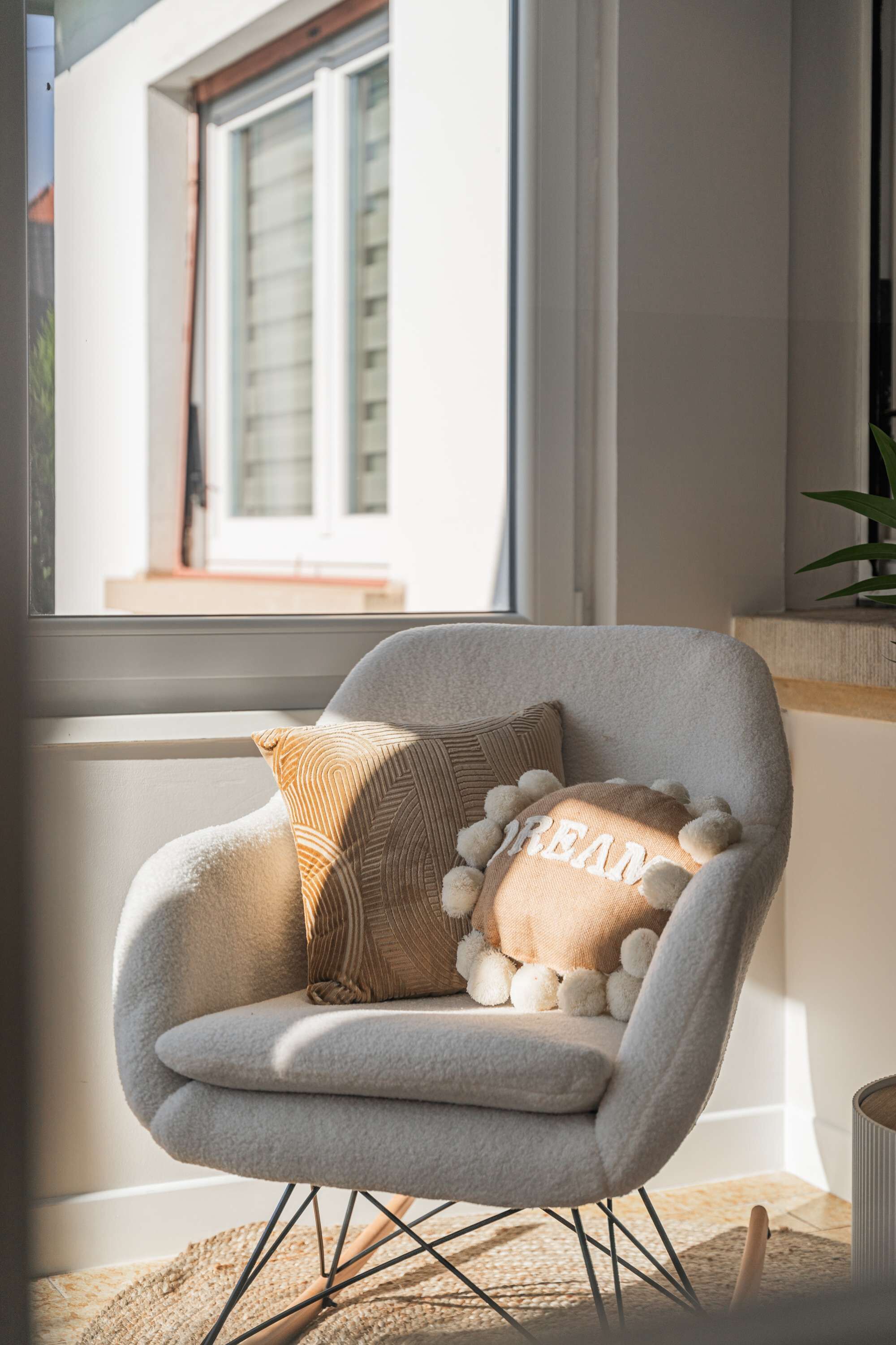 Uma poltrona moderna com um encosto almofadado que exibe a palavra 'Dream' e uma janela com persianas.