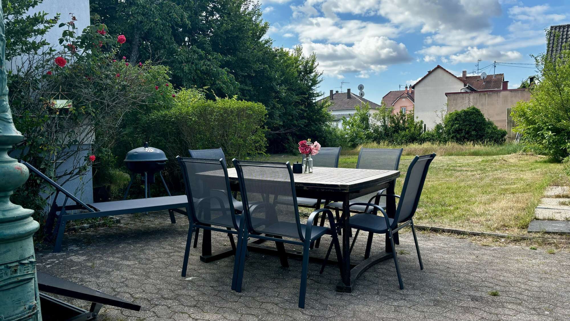 An outdoor patio with a table and chairs, surrounded by greenery and a view of houses.