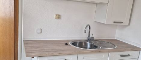 A compact kitchen with white cabinets, a stainless steel sink, and a wooden countertop.