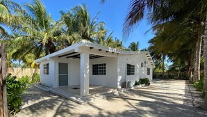 A white single-story house with a covered porch, surrounded by palm trees and a sandy driveway. - Casa de playa estilo California en Telchac puerto (Telchac Puerto)
