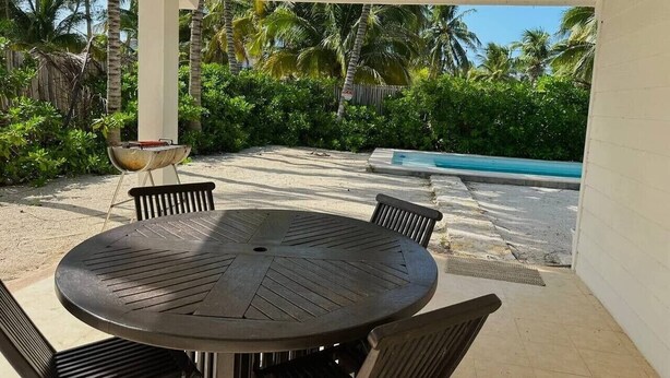 A covered outdoor area with a round table and chairs, a grill, and a pool in the background. - Casa de playa estilo California en Telchac puerto (Telchac Puerto)