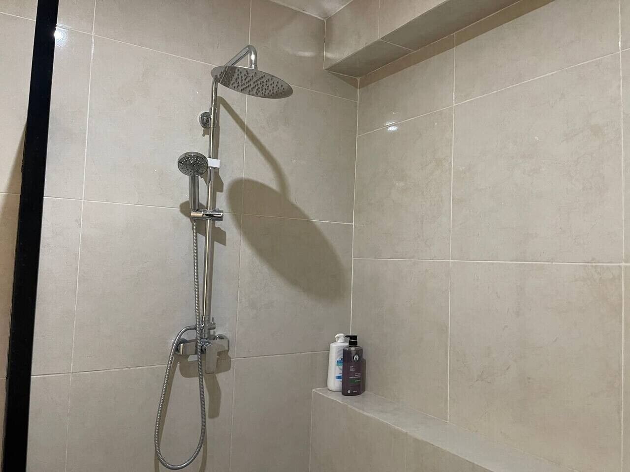 Een douche met een handdouche en een wandmengkraan, een plank met toiletartikelen, en een betegelde muur.