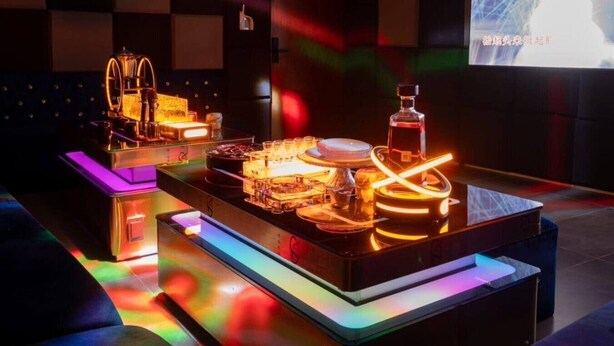 Un espace bar moderne, doté d’un comptoir éclairé par des néons, d’une grande sculpture lumineuse et d’un écran de télévision en arrière-plan.
