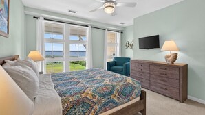 A bedroom with a bed, a chair, a dresser, a ceiling fan, and a TV.