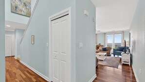 A hallway with a wooden floor, a white door, and a living area with a sofa and a TV.