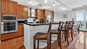 A modern kitchen with wooden cabinets, stainless steel appliances, a bar area with stools, and a view of the outdoors.