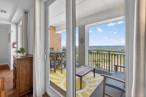 Un balcón con vista al mar, una mesa de madera, sillas y una planta pequeña.