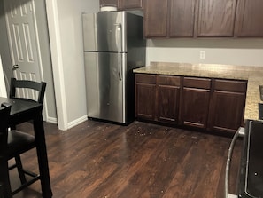 Eine Küche mit einem Edelstahl-Kühlschrank, Holzschränken, einer Arbeitsplatte aus Granit und einem dunklen Holzboden.