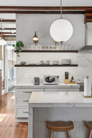 A modern kitchen with a marble countertop, a built-in microwave, and a hanging light fixture. - The Plunge at King Street w/ Private Pool (Charleston)