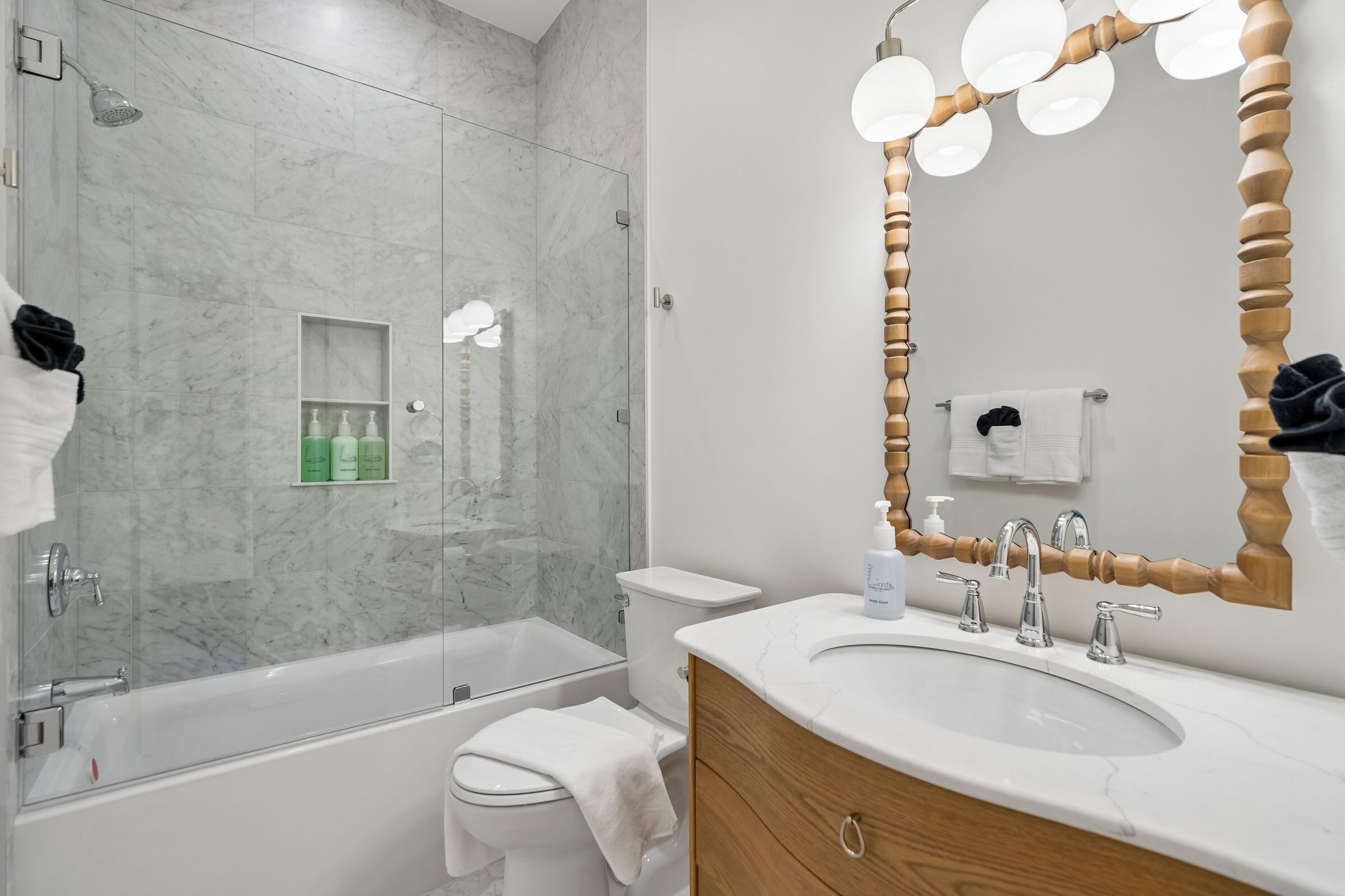 A modern bathroom with a glass shower enclosure, a white bathtub, a vanity with a sink, and a wooden-framed mirror.