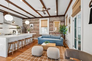 A modern kitchen with a marble countertop, wooden stools, and a blue sofa in a living area with a brick wall and wooden beams. - The Plunge at King Street w/ Private Pool (Charleston)