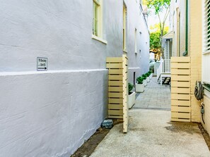 A narrow alleyway with a white building on one side and a wooden fence on the other. A sign indicates '78 Society Unit B'. - The Plunge at King Street w/ Private Pool (Charleston)
