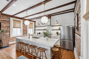 A kitchen with a large island, bar stools, a refrigerator, and a brick wall. - The Plunge at King Street w/ Private Pool (Charleston)