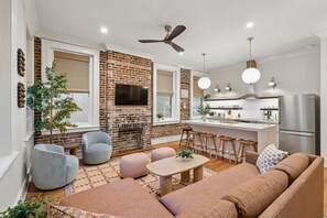 A modern living room with a fireplace, a kitchen with bar stools, and a ceiling fan. - Indigo Suite: Heart of Charleston w/ private pool (Charleston)