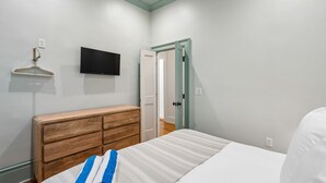 Quarto com cama, cômoda de madeira, televisão e porta para outro ambiente.