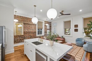 A modern kitchen with a marble island, a brick wall, and a ceiling fan. - Indigo Suite: Heart of Charleston w/ private pool (Charleston)
