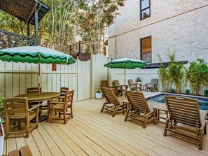 Eine Holzterrasse mit Gartenmöbeln, einem Pool und einem weißen Zaun.
