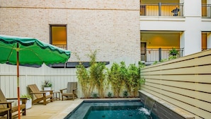 Piscina com cachoeira, rodeada por espreguiçadeiras de madeira e um guarda-sol verde.