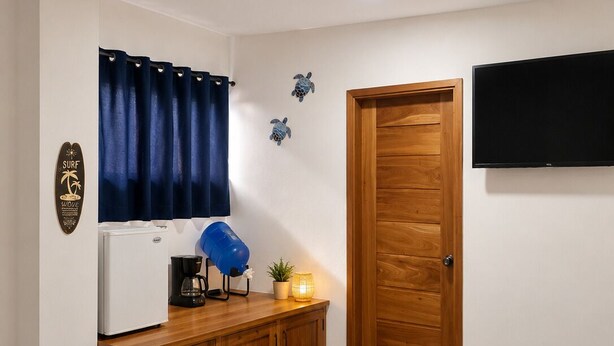 Une pièce comprenant un meuble en bois, une machine à café, une lampe bleue, une plante en pot, un téléviseur fixé au mur et une porte avec un cadre en bois.