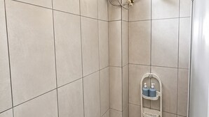 Un petit espace de douche carrelé, équipé d’un pommeau de douche à main, d’un distributeur de savon et d’un sèche-mains.
