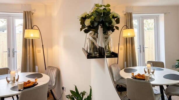 Un área de comedor con dos mesas redondas, sillas, un jarrón con flores y una lámpara.