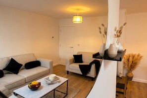 Ein modernes Wohnzimmer mit einer Couch, einem Sessel, einem Couchtisch und einem kleinen Beistelltisch mit Obstschale.
