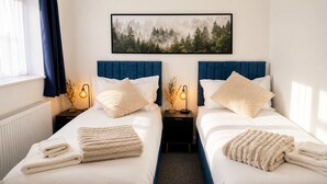 Habitación de hotel con dos camas, ropa de cama blanca, cabeceros azules y un cuadro con motivos de bosque.