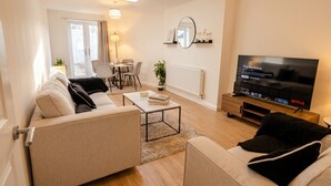 Una sala de estar moderna con sofá, mesa de centro, televisor y un comedor con sillas y una mesa.