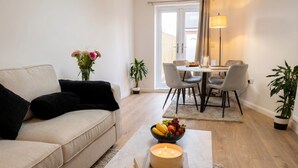 Una sala de estar moderna con un sofá, una mesa de centro con una vela, un frutero y un comedor con sillas y una mesa.