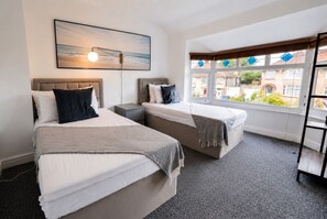 A hotel room with two beds, a window with a view, a painting on the wall, and a lamp.