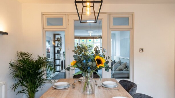 Una mesa de comedor lista para cuatro personas, con platos, cubiertos y un jarrón de flores.