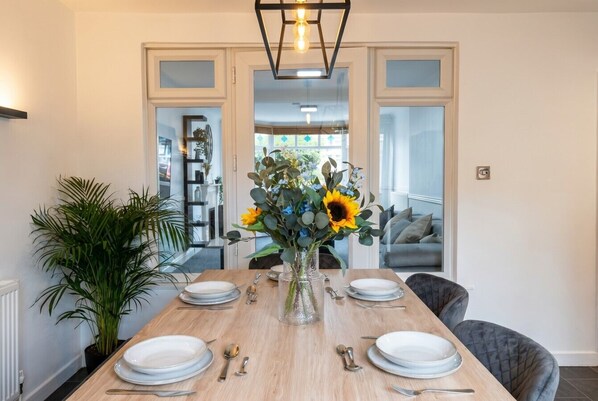 A dining table set for four with plates, cutlery, and a vase of flowers. - Pool Table & Free Parking · 4-Bed Home Sleeps 8 · Cowley, Oxford (Oxfordshire)
