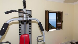 Een sportschool met een rode Weider bank, een optrekstang en een raam met uitzicht op zee.