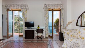 Een kamer met een televisie, een kleintje tafeltje, een bank en een balkon met gordijnen.