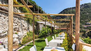 Een terras met tafels en stoelen, een pergola en een bergachtig landschap.