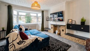 A modern living room with a sofa, a fireplace, a TV, and a window with curtains. - 4-Bed Headington Home · Sleeps 8 with Parking · Walk to JR Hospital (Headington)