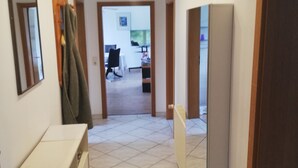 Un pasillo con suelo de baldosas, un perchero, un espejo y una puerta que da a una habitación.
