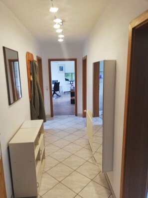 A hallway with a tiled floor, a coat rack, a mirror, and a door leading to a room. - Quiet vacation apartment in a village. Dogs welcome, fenced garden (Wittenburg)