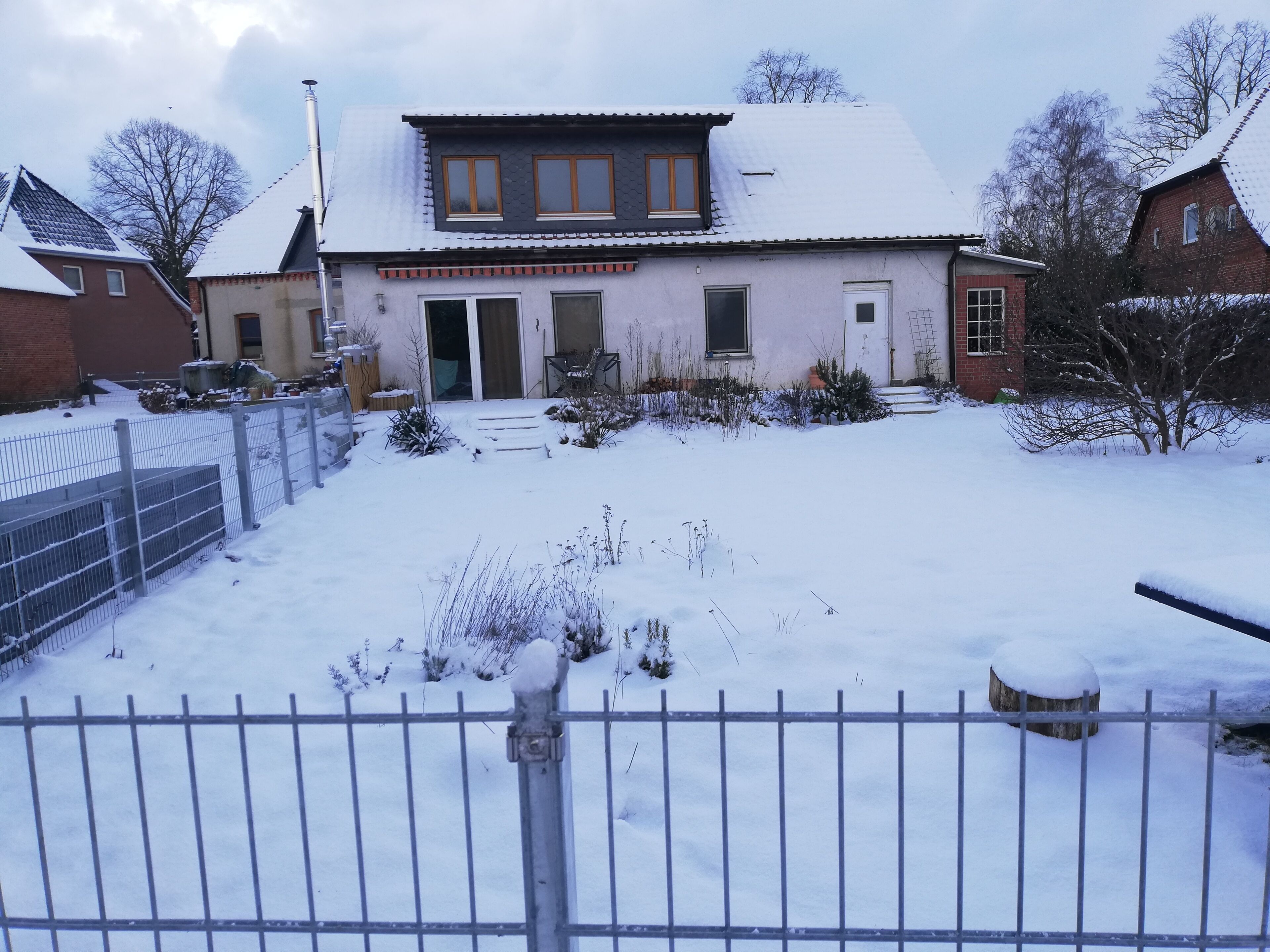 A residential building with a snow-covered roof, a front door, and a small garden area.