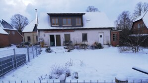 Un edificio residencial con techo nevado, puerta principal y un pequeño jardín.