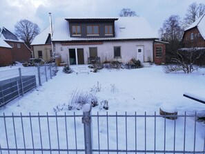 A residential building with a snow-covered roof, a front door, and a small garden area. - Quiet vacation apartment in a village. Dogs welcome, fenced garden (Wittenburg)